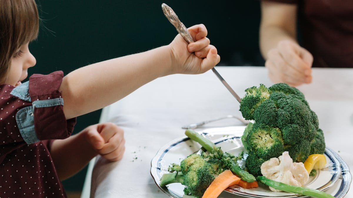 A child enthusiastically eating a plate full of fresh vegetables at the dining table.